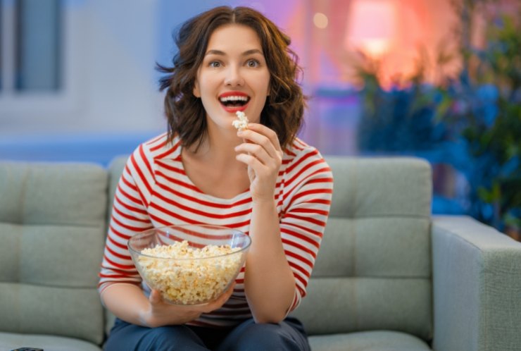 Donna guarda la TV mangiando Popcorn