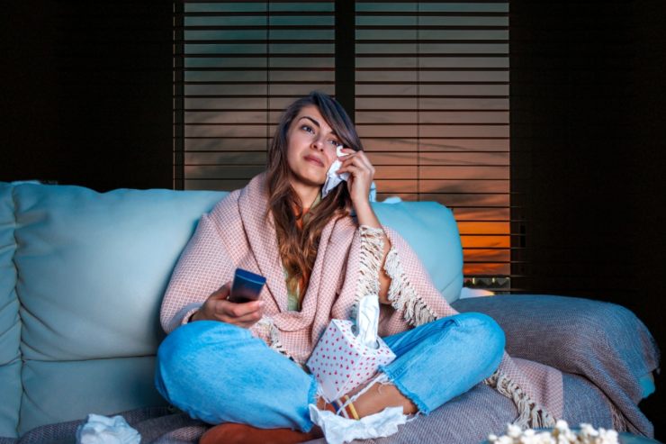 Una donna che guarda la TV commossa mentre si asciuga gli occhi in lacrime